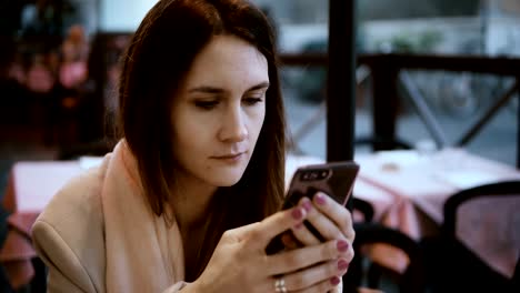 Young-brunette-woman-sitting-in-the-cafe-and-waiting-order.-Attractive-female-uses-the-smartphone,-surfing-the-Internet