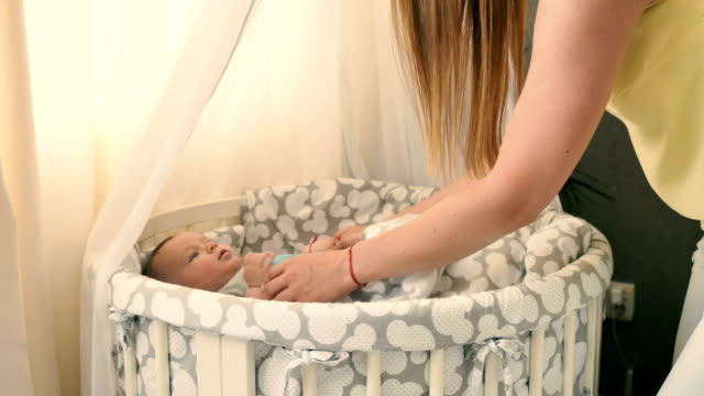 Young-mother-raises-up-her-baby-by-hands-to-put-him-in-crib