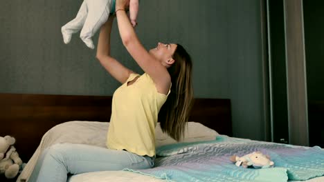 Junge-Mutter-sitzt-auf-dem-Bett-und-ihr-kleiner-Sohn-mit-Händen-aufrichten
