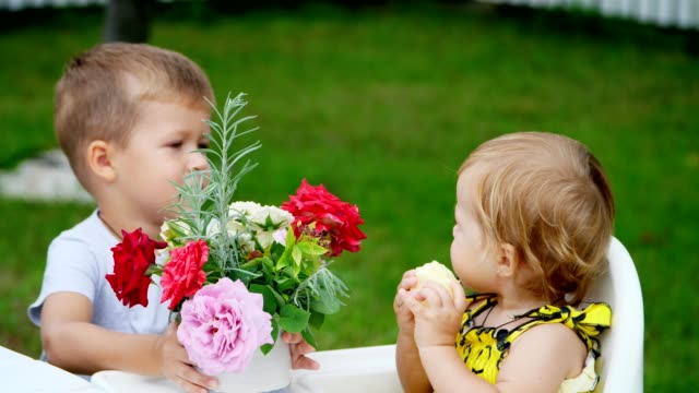 Sommer-im-Garten.-die-vier-jähriger-Junge-gibt-einen-Blumenstrauß-an-seine-jüngeren-ein-Jahr-alte-Schwester,-Bruder-Schwester-auf-die-Wange-küsst.-Das-Mädchen-isst-einen-Apfel