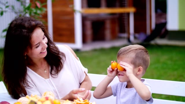 summer,-in-the-garden.-a-four-year-old-boy,-having-fun-with-his-family-outdoors,-twisting,-applying-mandarins-to-his-eyes.-family-holidays,-lunch-on-the-nature,-in-the-courtyard