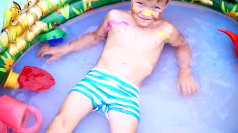un-niño-de-cuatro-años-de-edad-se-encuentra-en-la-piscina-inflable-para-niños,-salpicaduras-de-agua,-sonriendo.-Cerca-juguetes-de-flotador.-Ve-desde-arriba