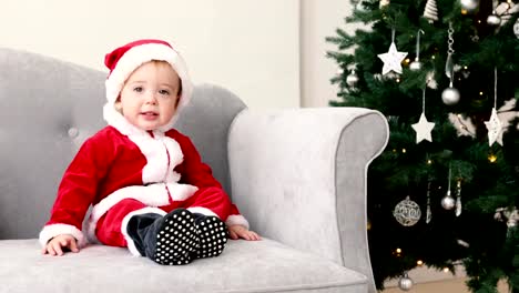Baby-in-Santa-Anzug-sitzen-auf-Sofa-mit-Weihnachtsbaum