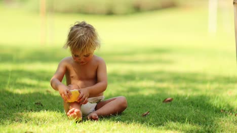Adorable-candid-cute-moment-of-infant-toddler-boy-playing-with-pear-fruit-while-sitting-in-the-grass-outdoors-in-the-sunlight-in-4k-clip-resolution
