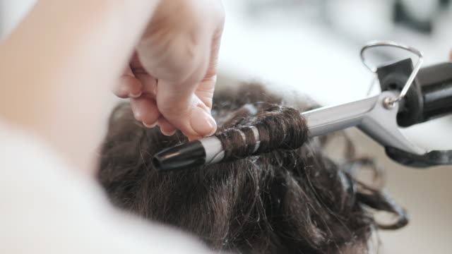 A-woman-in-a-hairdressing-salon.-Master-twisting-curls-on-short-haircut.-Only-hands.-Slow-motion