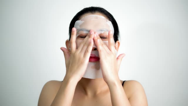Junge-Frau-tut-Gesichtsmaske-Blatt-mit-reinigende-Maske-auf-ihr-Gesicht-auf-weißem-Hintergrund