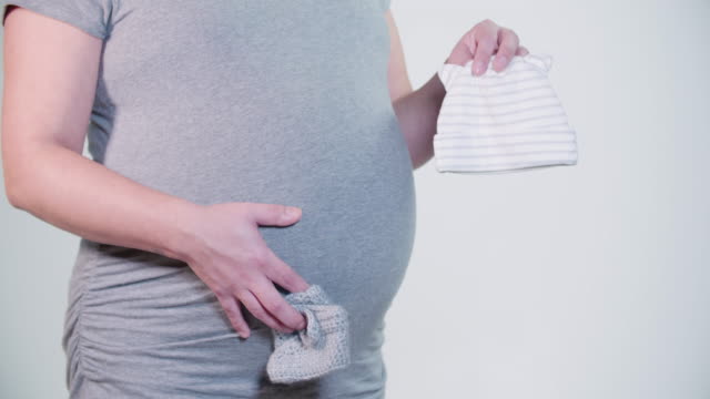 Madre-embarazada-celebración-bebé-botines-sombrero-en-las-manos-sobre-el-vientre-abultado