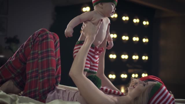 Schöne-Mutter-in-Weihnachten-Kleidung-ist-am-Bett-liegen-und-spielen-mit-ihrem-lächelnden-Baby-Sohn