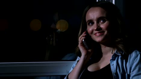 Eine-schwangere-Frau-in-der-Nacht-telefonieren-mit-einem-Handy-berühren-den-Bauch-mit-den-Händen-stehend-auf-das-große-Panoramafenster-mit-Blick-auf-die-Stadt