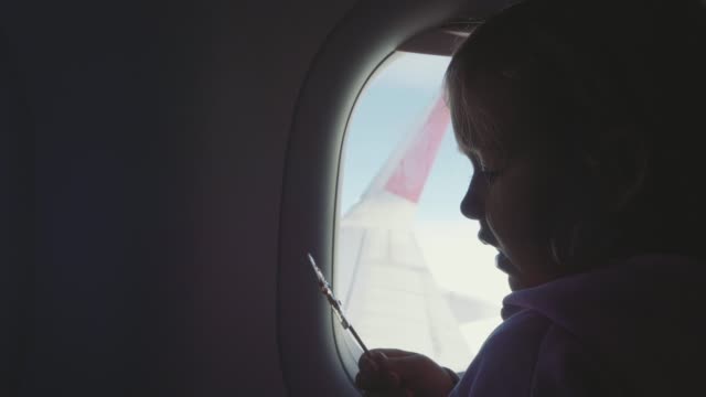 Silhouette-Kind-Mädchen-saugen-Süßigkeiten-auf-Holzstab-über-Bullauge-in-Flugzeug
