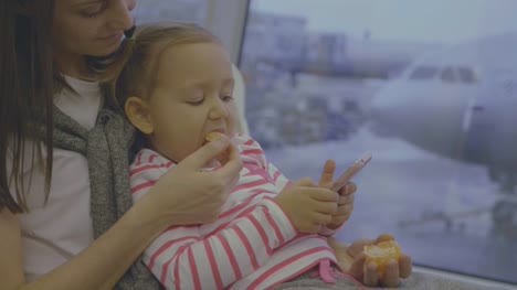 Mutter-füttert-ihr-Töchterchen-mit-Mandarine-am-Flughafen-in-Zeitlupe