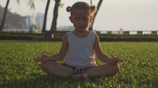 Kleine-süße-Mädchen-meditiert-in-türkischen-Pose-im-Park-bei-Sonnenuntergang.