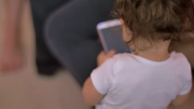 Ein-Kleinkind-ein-Handy-holt-und-beginnt-Knöpfe-drückt,-so-dass-der-Bildschirm-leuchtet