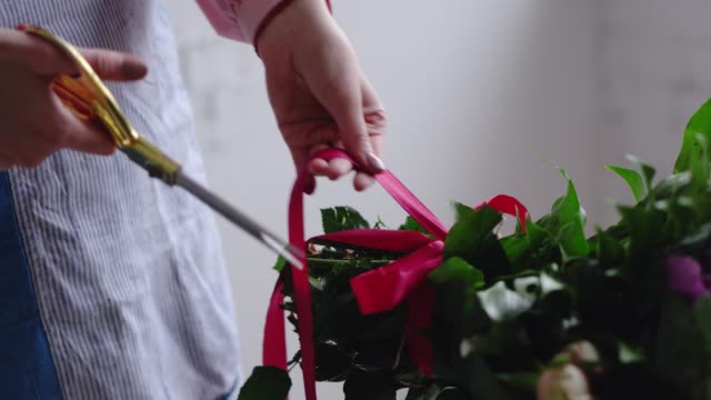 Blumengeschäft-schneidet-die-rote-Schleife-auf-das-Bouquet-mit-einer-Schere