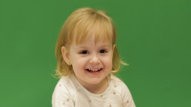 Cute-child-smiles-and-showing-her-tongue.-Beautiful-two-years-old-girl.-Cute-blonde-child.-Brown-eyes.-Close-up.-Green-screen-background