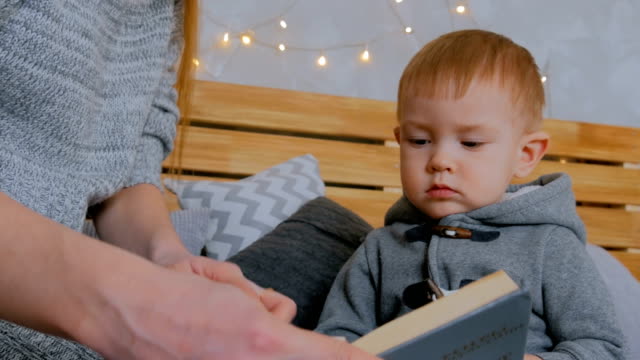 Young-mother-and-her-baby-son-reading-book-at-home