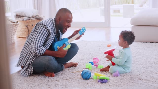 Young-black-father-palying-ukulele-with-son-in-sitting-room