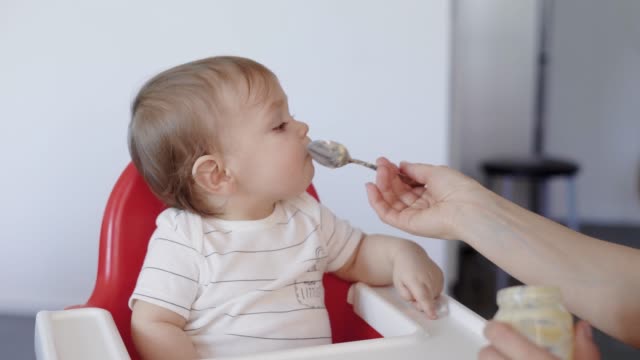 portrait-of-a-sweet-child,-who-is-fed-baby-food-from-a-spoon,-mother-feeds-her-son-with-delicious-food
