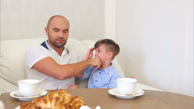 Junger-Vater-seinen-kleinen-Sohn-Gesicht-reinigen,-nach-dem-Mittagessen