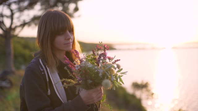 beautiful-young-woman-with-a-bouquet-of-wildflowers-on-the-coast-at-sunset