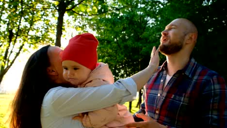 Happy-parents-play-with-a-child-in-a-close-up-park.-Young-family-with-little-baby-hugging-and-kissing-each-other-in-summer-park-at-sunset