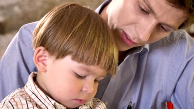 Junger-Vater-und-seinen-kleinen-Sohn-schreiben-auf-Papier-und-halten-Tablet,-Papa-helfen-und-sein-Sohn-beizubringen,-schreiben