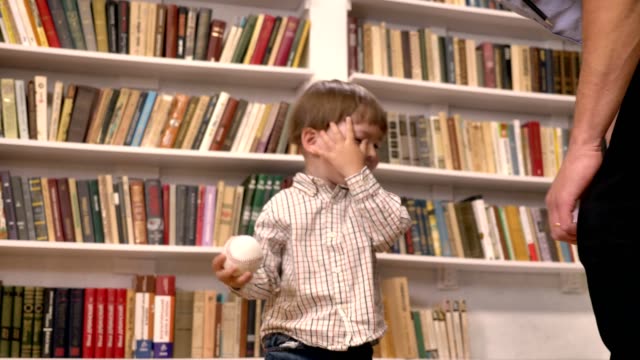 Young-father-and-his-little-son-playing-with-ball,-smiling,-happy,-shelves-with-books-background