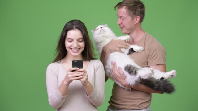 Young-couple-using-phone-together-with-cat-against-green-background