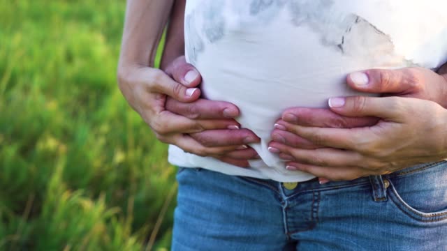 Closeup-of-parents-hands-touching-pregnant-belly-in-nature