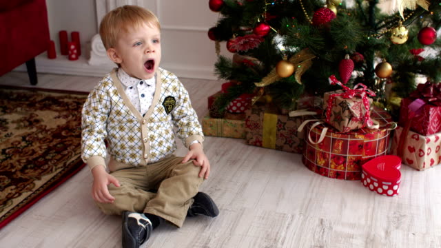 Child-is-sitting-near-the-Christmas-tree-and-yawns