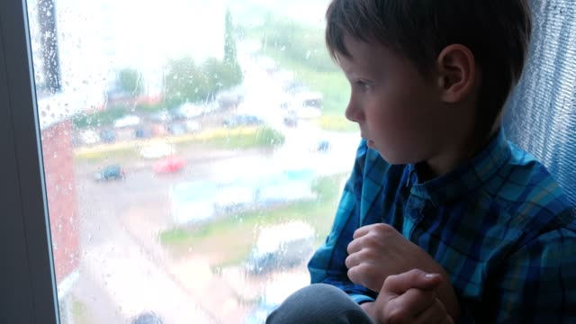 Boy-looks-out-the-window-in-the-rain-and-is-sad.