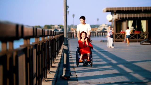 Rodillos-chico-A-discapacitados-a-una-niña-sonriente-con-el-pelo-rojo-en-una-silla-de-ruedas-en-el-paseo-marítimo