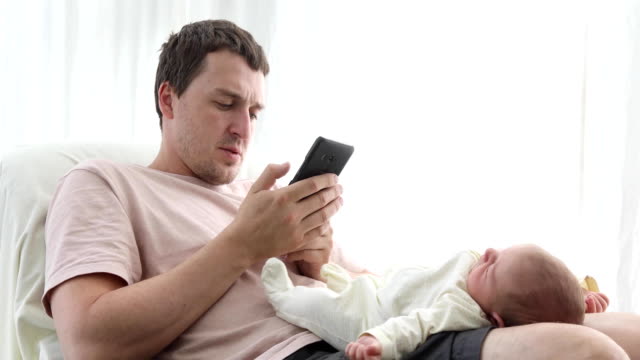 Mann-mit-Telefon-mit-Baby-auf-Knien-entspannen