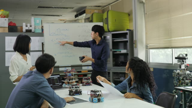 In-Computer-Science-Class-Teacher-talking-to-students-about-robot-technology.-Male-engineer-present-project-with-team.-People-with-technology-or-innovation-concept.