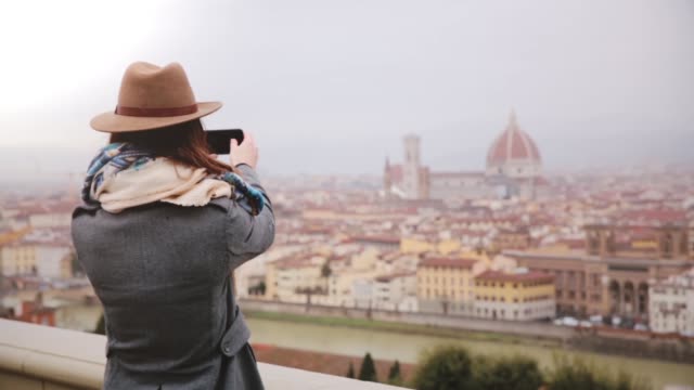 Cheerful-tourist-girl-taking-smartphone-photo-at-amazing-cityscape-panorama-of-autumn-Florence,-Italy,-walking-away.