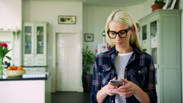 Attraktive-blonde-Frau-SMS-auf-Smartphone-im-Home-Office