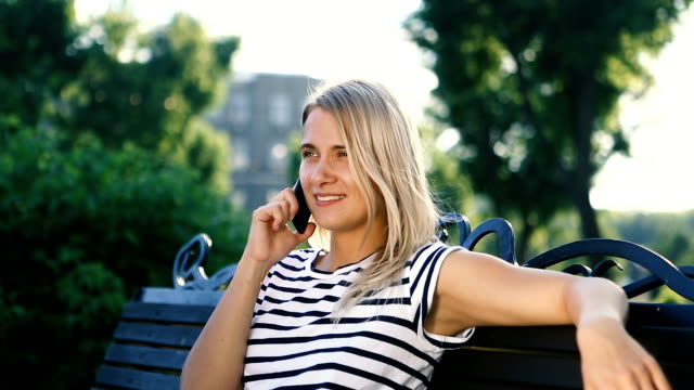 Attraktive-blonde-junge-Frau-sitzt-im-Park-telefonieren-mit-ihrem-Handy