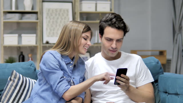 Joven-pareja-utilizando-Smartphone-mientras-relajante-en-el-sofá,-mensajería
