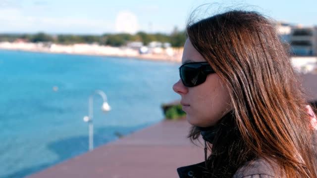Junge-Brünette-Frau-mit-Sonnenbrille-mit-Blick-auf-das-Meer-im-Herbst.