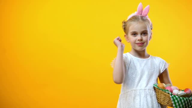 Happy-Easter-text,-cute-child-with-eggs-basket-in-bunny-ears-showing-thumbs-up