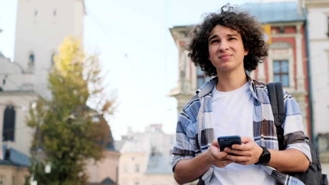 Attraktiver-junger-Mann,-Tourist-oder-Student,-Generation-z-oder-Millennial-im-Hipster-Outfit,-Überprüfung-von-Mails,-abgelenkt-durch-soziale-Medien-oder-Spiele-Anwendungen,-starrt-in-Newsfeed-auf-dem-Smartphone