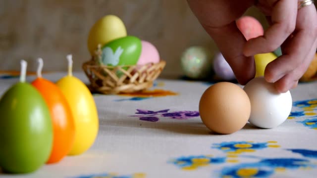 Happy-Easter.-male-hand-turns-a-white-chicken-egg-on-the-table.-olorful-Easter-eggs-in-the-background.