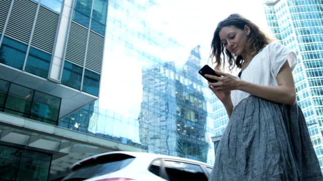 Woman-uses-a-smartphone-on-the-background-of-business-centers-on-the-street
