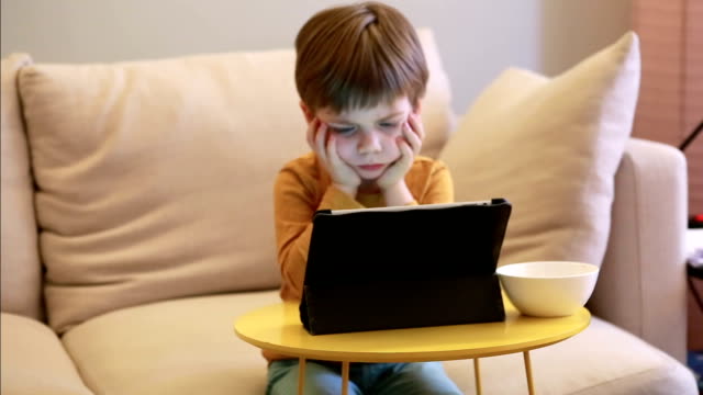 Child-using-tablet-pc-on-bed-at-home.-Cute-boy-on-sofa-is-watching-cartoon,-playing-games-and-learning-from-laptop.-Education,-fun,-leisure,-happiness,-modern-computer-technology-and-communication.