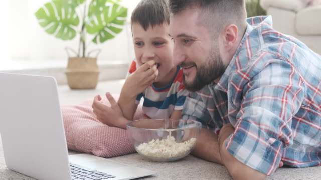 Vater-mit-Sohn-essen-Popcorn,-während-man-lustigen-Film-auf-dem-Laptop-sieht