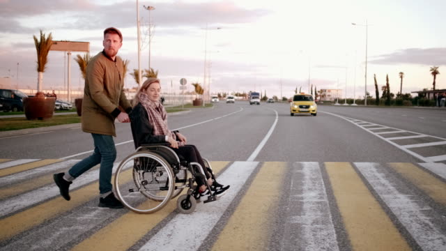 Mann-entfernt-behinderte-Frau-in-Wagen-über-Fußgängerüberweg-in-der-Stadt