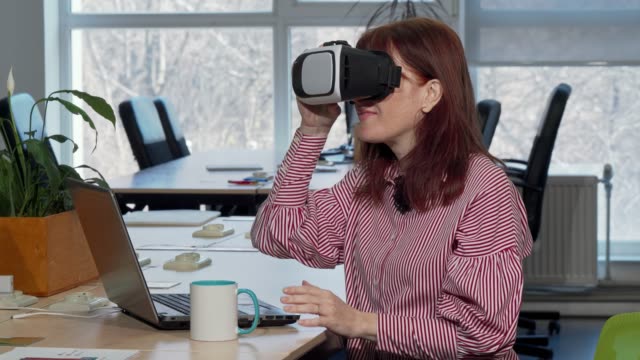 Mature-businesswoman-enjoying-using-virtual-reality-headset-at-her-workplace