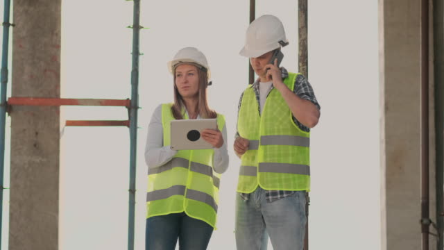 The-controller-is-a-man-of-a-building-under-construction-talking-on-the-phone-with-management-and-has-discussed-with-the-engineer-and-architect-woman-construction-progress