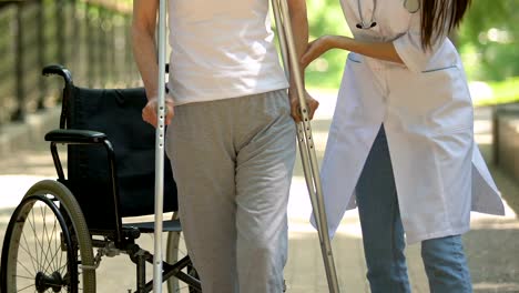 Physiotherapist-helping-patient-on-wheelchair-rising-and-walking-with-crutches