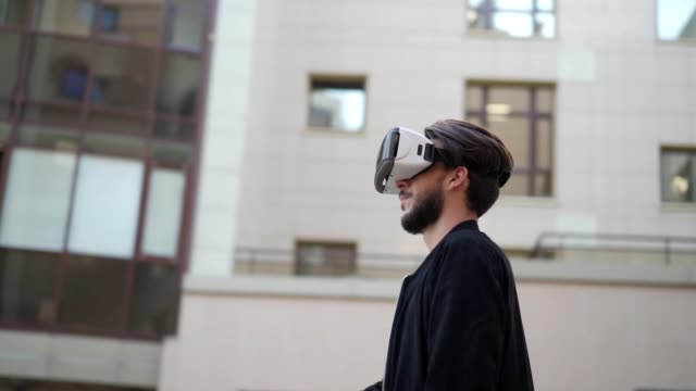 Panning-slow-motion-shot-of-young-man-in-vr-headset-standing-in-street-and-exploring-data-visualized-in-virtual-reality.-Man-swiping-and-magnifying-information